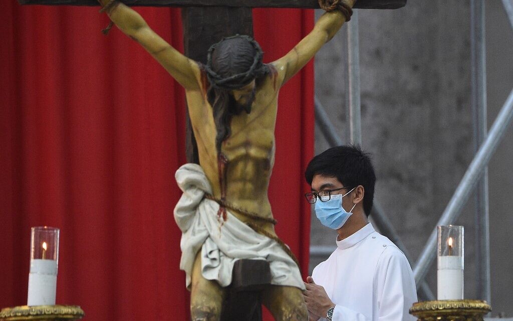 Un enfant de chœur portant un masque se tient à côté d'un crucifix dans une église du Saint-Rosaire vide, avec des photos de paroissiens posées sur des bancs d'église (non illustrés), dans le cadre des mesures de distanciation sociale en pleine pandémie de COVID-19, pendant la Messe du dimanche de Pâques à Angeles City, aux Philippines, le 12 avril 2020. (Crédit : Ted ALJIBE / AFP)