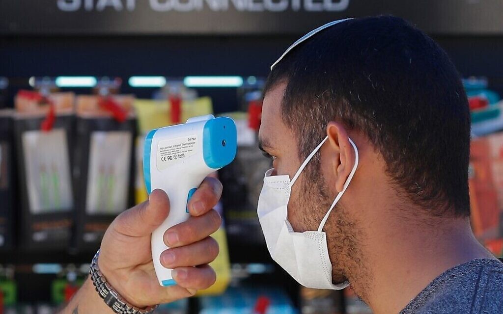 Un employé contrôle la température d'un client avant qu'il n'entre dans un magasin de Jérusalem, le 20 avril (Crédit : Emmanuel Dunand/AFP)