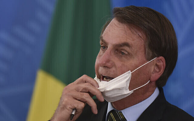 Le président brésilien Jair Bolsonaro enlève son masque pour s'adresser aux journalistes après une conférence de presse sur le nouveau coronavirus, au Palais présidentiel Planalto à Brasilia, Brésil, le 18 mars 2019. (Crédit : AP Photo/Andre Borges)