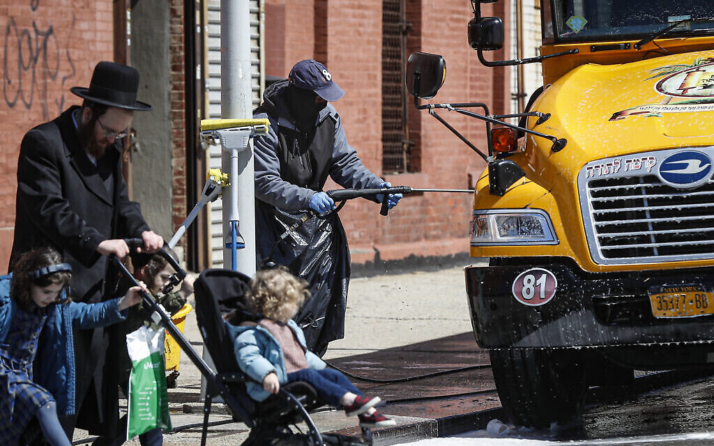 Un employé portant un équipement de protection individuelle lave un bus scolaire qui dessert une communauté juive ultra-orthodoxe dans le quartier de Brooklyn à New York, le 27 mars 2020. (AP Photo/John Minchillo)