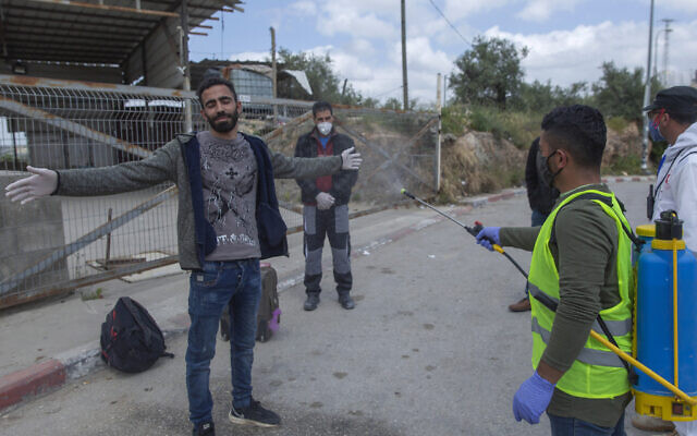 Un personnel soignant du ministère palestinien de la Santé désinfecte des travailleurs palestiniens pour tenter de contenir la pandémie de coronavirus à leur retour d'Israël, à proximité du village de Nilin, en Cisjordanie, à l'ouest de Ramallah, le 7 avril 2020. (Crédit : AP Photo/Nasser Nasser)