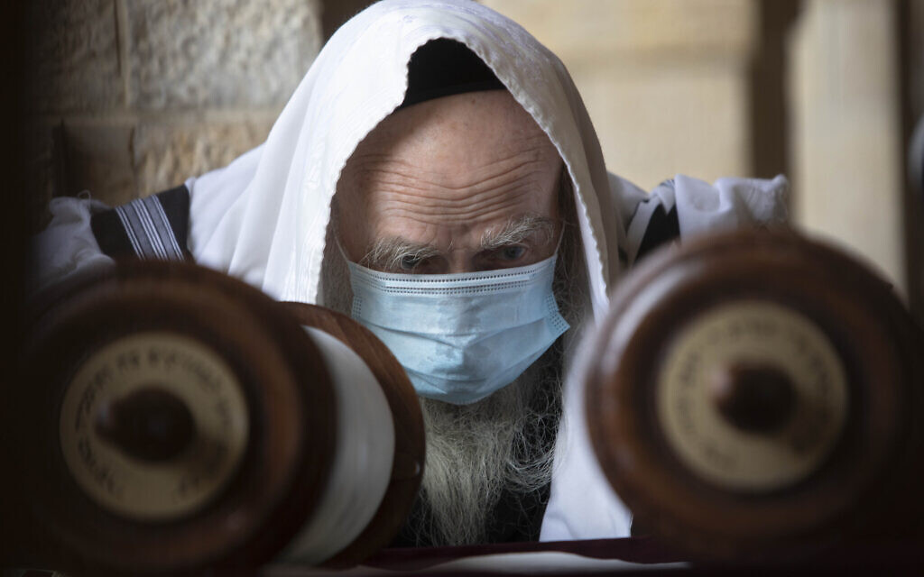 Un homme juif porte un masque sur le visage pour éviter la propagation du coronavirus alors qu'il lit un rouleau de Torah au mur Occidental, dans la Vieille Ville de Jérusalem, le 10 avril 2020 (Crédit : AP Photo/Sebastian Scheiner)