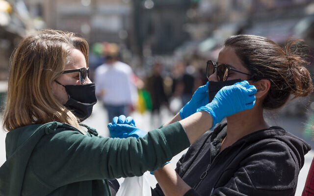 Des femmes s'entraident pour revêtir des masques au marché de Mahane Yehuda (Nati Shohat/Flash90)