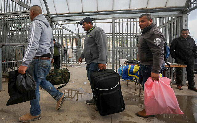Des ouvriers palestiniens de la ville de Hébron en Cisjordanie portent leurs affaires personnelles en arrivant au point de passage de Tarqumiya pour entrer en Israël, le 18 mars 2020. (Wisam Hashlamoun/Flash90)
