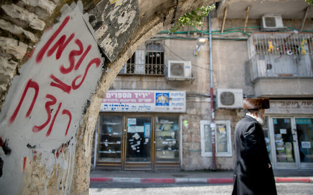 Un homme ultra-orthodoxe passe à côté d'un graffiti contre le ministre de la Santé Yaakov Litzman dans le quartier de Mea Shearim à Jérusalem le 12 avril 2020. On peut lire sur le graffiti "Litzman = meurtrier". (Yonatan Sindel/Flash90)