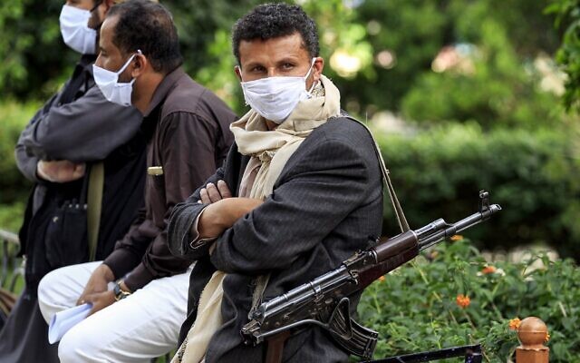 Un combattant appartenant aux rebelles houthis du Yémen porte un masque facial et des gants en latex et en lançant un fusil d'assaut à kalachnikov. Ces volontaires font partie d'une initiative communautaire visant à prévenir la propagation du COVID-19 qui se propage dans la capitale du Yémen, Sanaa, le 14 mai 2020. (Crédit :  MOHAMMED HUWAIS / AFP)