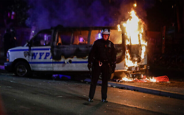 Un officier de police regarde la foule alors qu'un véhicule de police brûle lors de manifestations contre la mort de George Floyd à Brooklyn, New York, le 29 mai 2020. (Crédit : AP / Frank Franklin II)