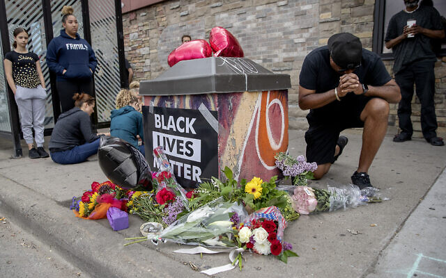 Les gens se rassemblent et prient autour d'un mémorial improvisé, le 26 mai 2020, à Minneapolis, près du site où un homme noir, qui avait été placé en garde à vue la veille, est mort. (Crédit : Elizabeth Flores/Star Tribune via AP)