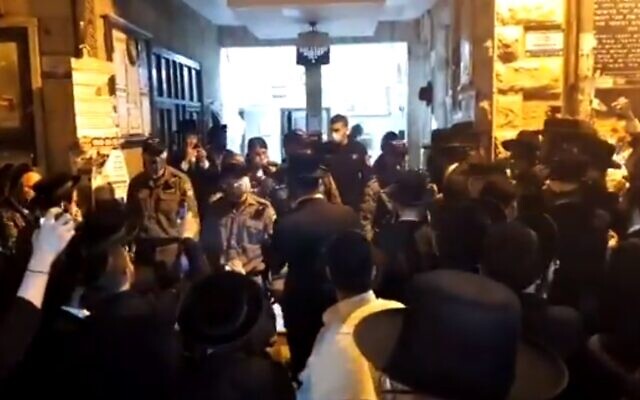 Des dizaines de personnes rassemblées lorsque la police arrive pour disperser la foule qui enfreint la réglementation sur le coronavirus dans une synagogue du quartier ultra-orthodoxe de Mea She'arim à Jérusalem, le 15 mai 2020 (Capture d'écran/Kan)