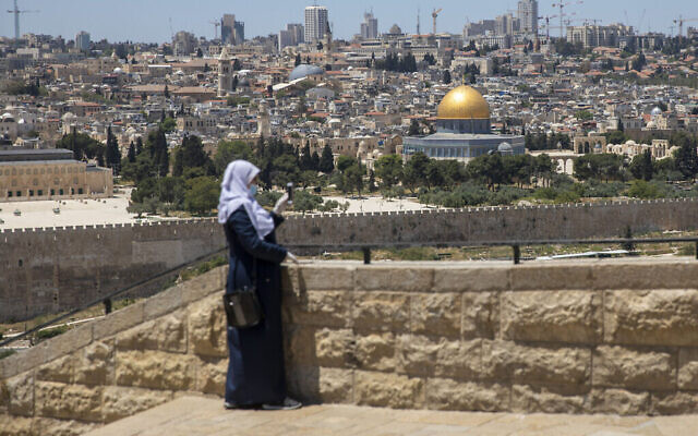 Une femme musulmane porte un masque et des gants sur le Mont des Oliviers à Jérusalem-Est, qui surplombe le Dôme du Rocher et le complexe de la mosquée Al-Aqsa sur le Mont du Temple, qui reste fermé pour empêcher la propagation du coronavirus pendant le mois sacré du Ramadan, le vendredi 1er mai 2020. (AP Photo/Ariel Schalit)