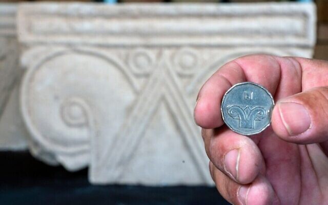 Une pièce de cinq shekels juxtaposée à une tête de colonne trouvée à Armon HaNatziv (Yaniv Berman, Autorité des antiquités d'Israël)