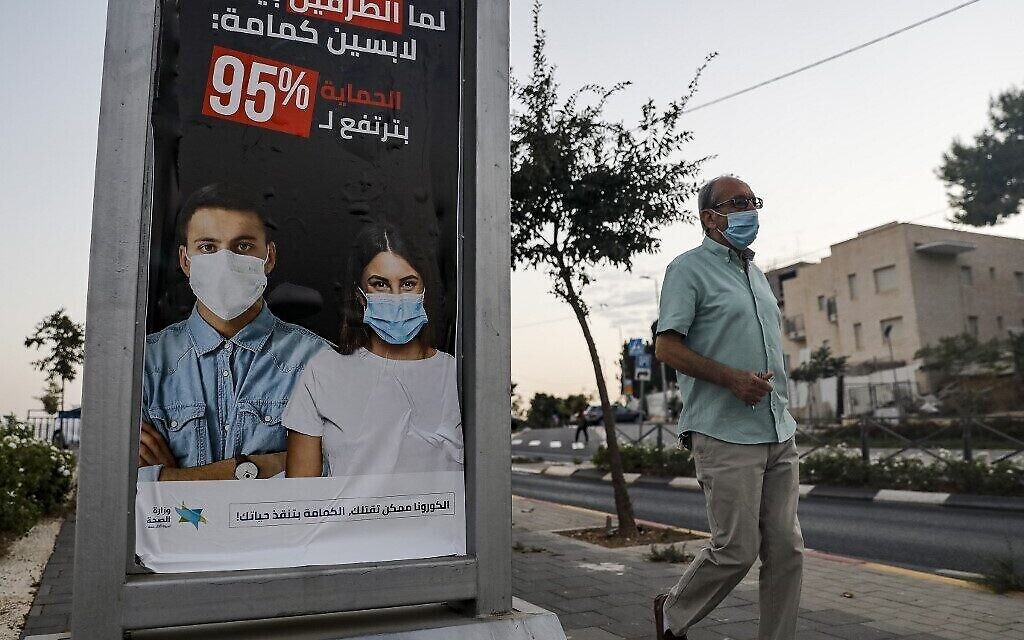 Un homme passe devant un panneau publicitaire avec une affiche du ministère israélien de la Santé qui demande aux gens de porter des masques faciaux en arabe comme méthode de prévention de la COVID-19 dans le quartier arabe de Sheikh Jarrah à Jérusalem-Est, le 8 octobre 2020. (Photo d'Ahmad GHARABLI / AFP)