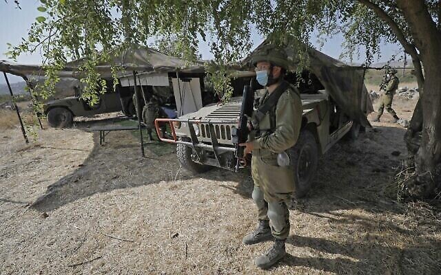 Un soldat israélien, masqué en raison de la pandémie de coronavirus COVID-19, monte la garde à côté d'un avant-poste et de véhicules militaires de transport à roues polyvalents (Humvee) lors de l'exercice militaire "Deadly Arrow" dans le nord d'Israël, le 27 octobre 2020. (Crédit : Jalaa Marey/AFP)