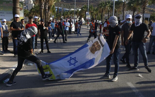 Des Palestiniens avec une bannière montrant le prince d'Abu Dhabi  Mohammed bin Zayed al-Nahyan arborant un drapeau israélien lors d'un rassemblement contre l'accord de normalisation des liens conclu entre Israël et les Emirats arabes unis, à  Turmusaya près de Ramallah, en Cisjordanie, le 19 août 2020. (Crédit : AP Photo/Majdi Mohammed)