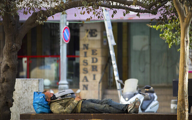 Un homme dort sur un banc public près de magasins fermés dans la rue Hillel, au centre de Jérusalem, pendant le confinement national, le 23 septembre 2020. (Crédit : Nati Shohat/Flash90)