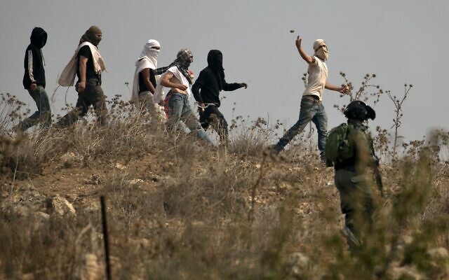 Des soldats israéliens se tiennent prêts alors que des habitants d’implantations israéliens masqués lancent des pierres sur des manifestants palestiniens (non vsisibles) qui se rassemblent lors d'une manifestation contre la construction d'un avant-poste israélien près du village palestinien de Turmusaya et de l’implantation de Shilo, au nord de Ramallah en Cisjordanie, le 17 octobre 2019. (JAAFAR ASHTIYEH/AFP)