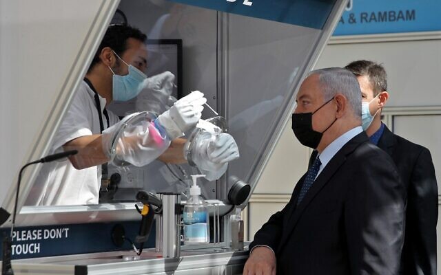Le Premier ministre Benjamin Netanyahu, portant un masque, assiste à une démonstration de prélèvement de coronavirus par écouvillonnage lors de l'inauguration d'un centre de dépistage rapide du coronavirus COVID-19 à l'aéroport international Ben Gurion de Lod, le 9 novembre 2020. (ATEF SAFADI / POOL / AFP)
