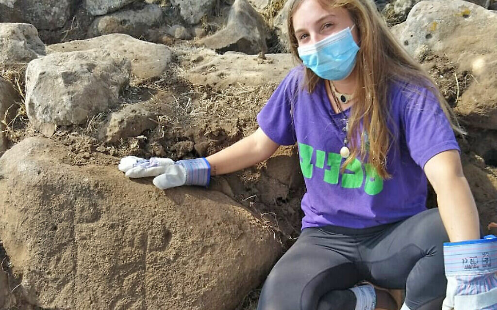 Ofri Eitan, de l'académie pré--militaire Kfar Hanasi, à côté de la pierre gravée découverte près d'Hispin dans le Golan et remontant au 11e siècle avant l'ère commune environ. (Crédit : Tidhar Moav, Autorité des Antiquités israélienne)