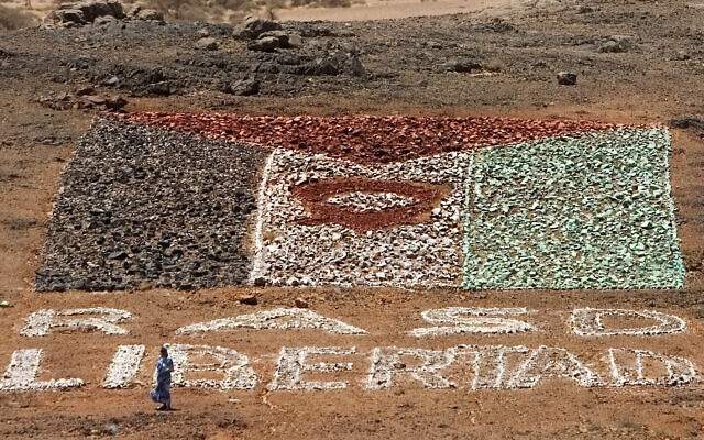 Une femme soutenant les soldats rebelles du Front Polisario pro-indépendance marche près d'un drapeau de fortune du Sahara occidental en pierres peintes sur lesquelles ont peut lire : République arabe sahraouie démocratique, ou RASD, libre" dans le désert près de Tifariti, le 20 mai 2008. (Crédit : Daniel Ochoa de Olza/AP)
