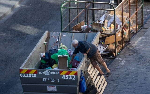Un homme fouille dans une belle à ordures dans le centre de Jérusalem, le 17 août 2020. (Crédit : Yonatan Sindel/Flash90)