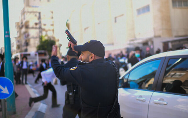 Un policier pointe son arme en l'air lors d'un affrontement avec des émeutiers ultra-orthodoxes qui protestaient contre l'application d'un confinement ordonné en raison du coronavirus, dans la ville de Bnei Brak, le 24 janvier 2021. (Tomer Neuberg/Flash90)