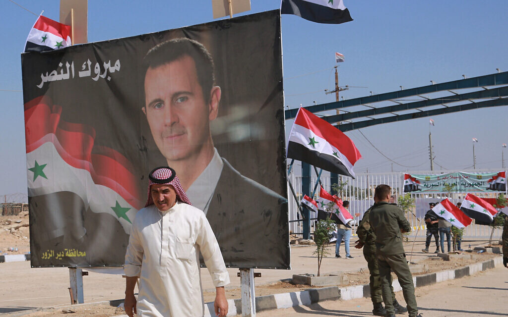 Un homme passe devant une affiche présentant le président syrien Bashar el-Assad en franchissant la frontière, au point de passage situé entre la ville de Qaim (Irak) et Boukamal (Syrie), le 30 septembre 2019. (Crédit : AP Photo/Hadi Mizban, File)