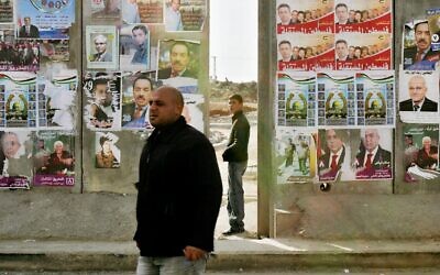 Un Palestinien passe devant une section de la barrière de sécurité israélienne couverte d'affiches de campagne pour les prochaines élections parlementaires palestiniennes dans le village cisjordanien d'A-Ram, dans la banlieue de Jérusalem, le 23 janvier 2006. (AP/ Oded Balilty)