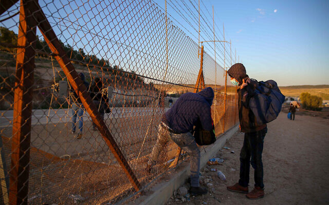 Des travailleurs palestiniens de Hébron, en Cisjordanie, avec leurs effets personnels, entrent sur le territoire israélien à travers un trou creusé dans la clôture de sécurité, aux abords de Hébron, le 31 janvier 2021. (Crédit : Wisam Hashlamoun/Flash90)