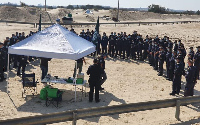 Des policiers reçoivent des instructions à la plage de Nitzanim, dans le sud d'Israël, avant de rejoindre des bénévoles pour aider à nettoyer le goudron d'une marée noire, le 22 février 2021 (Crédit : Menachem Fried/Autorité de la Nature et des Parcs)