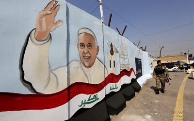 Un membre des forces irakiennes passe devant une peinture murale représentant le pape François saluant à côté d'un drapeau national irakien dessiné sur un mur anti-explosion devant l'église catholique syriaque de Notre-Dame de la Délivrance, dans le quartier de Karrada à Bagdad, la capitale irakienne, le 1er mars 2021, alors que les préparatifs de la visite du pontife sont en cours. (Crédit : Sabah ARAR / AFP)