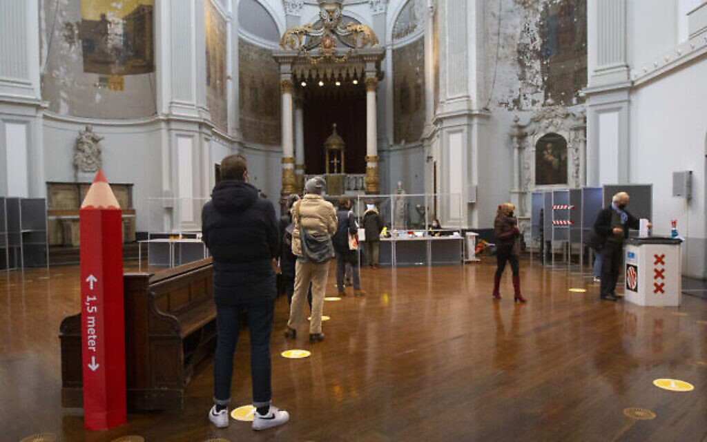 Un crayon rouge rappelle aux personnes qui font la queue pour voter de respecter la distanciation sociale d'un mètre et demi dans un bureau de vote installé dans l'église de De Duif à Amsterdam, aux Pays-Bas, le 15 mars 2021. (Crédit : AP Photo/Peter Dejong)