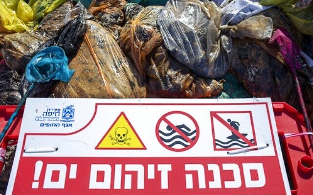 Un panneau qui dit "Danger, mer polluée" , près de sacs remplis de goudron collecté par les bénévoles suite à une marée noire en mer Méditerranée, sur une plage de Haïfa, dans le nord d'Israël, le 28 février 2021. (Crédit : Ariel Schalit/AP Photo)