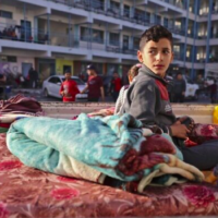 Un garçon palestinien qui a fui son domicile en raison des frappes aériennes israéliennes, menées en guise de représailles aux pluies de roquettes des groupes terroristes palestinien de Gaza visant Israël, est assis sur un matelas devant une école accueillant des réfugiés dans la ville de Gaza, le 14 mai 2021 (Crédit : MOHAMMED ABED / AFP)
