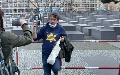 Un homme manifeste contre les restrictions entraînées par le coronavirus avec une étoile jaune et une photo d'Anne Frank aux abords du mémorial de la Shoah, à Berlin. (Crédit :  @ZSKberlin/Twitter via JTA)