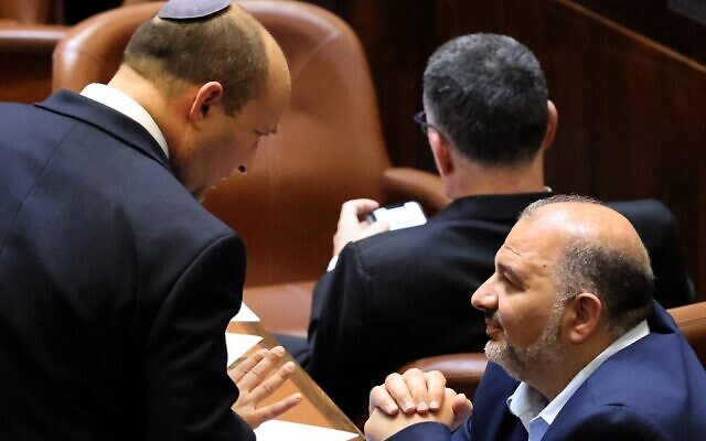 Le nouveau Premier ministre israélien Naftali Bennett (G) discute avec Mansour Abbas, chef du parti islamiste Raam, lors d'une session spéciale de vote pour le nouveau gouvernement à la Knesset, à Jérusalem, le 13 juin 2021. (Crédit : EMMANUEL DUNAND/AFP)