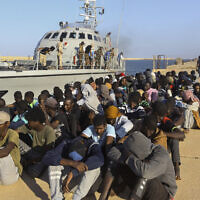 Dans cette photo d'archive du mardi 1er octobre 2019, des migrants secourus sont assis à côté d'un bateau des garde-côtes dans la ville de Khoms, en Libye, à environ 120 kilomètres à l'est de Tripoli. Les enquêteurs mandatés par l'organe suprême des droits de l'homme des Nations Unies pour examiner d'éventuels abus ont déclaré le 4 octobre 2021 avoir trouvé des preuves d'éventuels crimes de guerre et crimes contre l'humanité en Libye, en particulier contre des migrants cherchant à utiliser le pays agité d'Afrique du Nord comme moyen de se rendre en Libye. (Crédit : AP Photo/Hazem Ahmed, dossier)