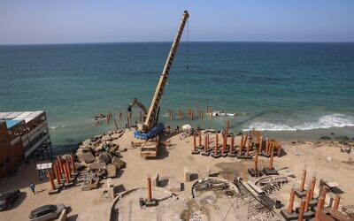 Une grue est utilisée pour déployer des échasses pour la construction d'une nouvelle jetée et d'un bâtiment de restauration le long du bord de mer méditerranéen dans la ville de Gaza, le 27 octobre 2021. (Crédit : MOHAMMED ABED / AFP)