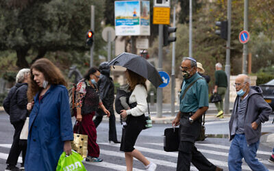 Des Israéliens portant des masques se protègent de la pluie sur Jaffa Road, à Jérusalem, le 31 octobre 2021. (Crédit : Olivier Fitoussi/Flash90)
