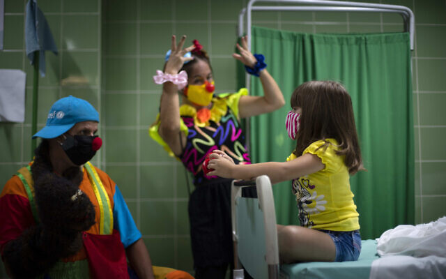 Des clowns divertissent une fillette qui attend dans la salle de contrôle après s'être fait injecter une dose du vaccin Soberana-02 contre le COVID-19 à La Havane, Cuba, le 24 août 2021. (Crédit :AP Photo/Ramon Espinosa)