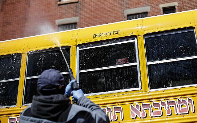 Illustration : Un travailleur couvert d'un équipement de protection individuelle lave un bus scolaire qui dessert une communauté juive ultra-orthodoxe dans l'arrondissement de Brooklyn à New York, le 27 mars 2020. (AP Photo/John Minchillo)