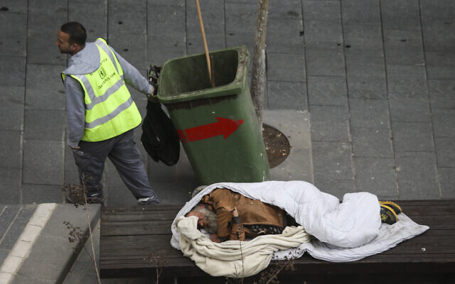 Un éboueur de la ville passe devant un sans-abri dormant sur un banc dans le centre de Jérusalem. 15 mars 2015. (Crédit : Nati Shohat/FLASH90)