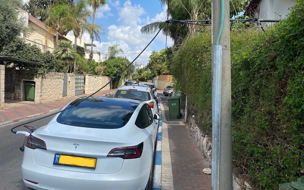 Une voiture Tesla est rechargée par le biais d'un système artisanal de câbles provenant de l'intérieur d'une habitation de Ramat Gan jusqu'à une place publique de stationnement, le 8 décembre 2021. (Autorisation : Sharon B.)