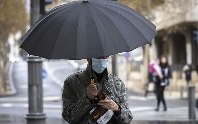 Un homme portant un masque s'abrite de la pluie sur la route de Jaffa dans le centre ville de Jérusalem, le 21 décembre 2021. (Olivier Fitoussi/Flash90)