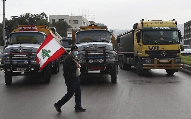 Un chauffeur de camion tient un drapeau libanais alors que d'autres chauffeurs bloquent une autoroute principale avec leurs véhicules pendant une grève générale des transports publics et des syndicats de travailleurs, à Beyrouth, au Liban, jeudi 13 janvier 2022. (Crédit : AP Photo/Bilal Hussein)