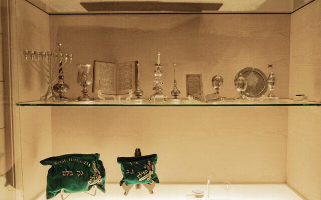 Une exposition d'objets religieux juifs traditionnels, dont une ménorah, des chandeliers, un Tanakh centenaire et l'exemplaire personnel du "Livre des Psaumes" de feu Jacob Ballas, ainsi que son tallit et son ensemble de tefillin. (Crédit : Jewish Welfare Board of Singapore/ via JTA)