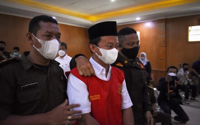 L'enseignant indonésien Herry Wirawan (C) est escorté avant son procès au tribunal de Bandung, dans l'ouest de Java, le 15 février 2022, où il a ensuite été condamné à la prison à vie pour le viol de 13 élèves, toutes mineures. (Crédit : TIMUR MATAHARI / AFP)