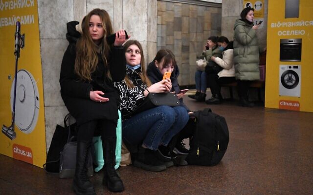 Des jeunes filles tiennent leur téléphone portable alors qu'elles se réfugient dans une station de métro à Kiev, dans la matinée du 24 février 2022. (Crédit : Daniel LEAL / AFP)