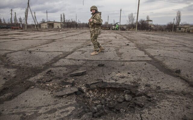 Un soldat ukrainien regarde un trou formé par un obus tiré par les séparatistes pro-russes dans le village de Novoluhanske, dans la région de Luhansk, en Ukraine, le 19 février 2022. (Crédit : AP Photo/Oleksandr Ratushniak)