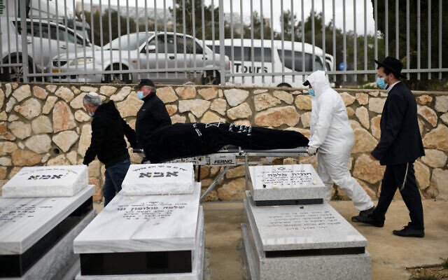 Un employé des services funéraires porte le corps de la survivante de la Shoah d'origine roumaine Golda Schwartz, décédée à l'âge de 93 ans des complications de la COVID-19, au cimetière Nof Hagalil, le 28 janvier 2021. (Crédit : Gili Yaari / Flash90)
