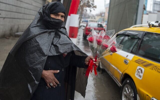 Une femme s'abrite de la pluie avec une bâche en plastique tout en vendant des fleurs le long d'une rue à l'occasion de la Journée internationale de lutte pour les droits des femmes à Kaboul, le 8 mars 2022. (Crédit :  Wakil KOHSAR / AFP)